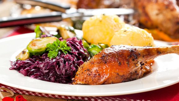 Gebratene Martinigans mit Rotkohl und Kartoffelknödeln auf einem weißen Teller, serviert auf einem rustikalen Holztisch mit rot-weiß karierter Tischdecke.